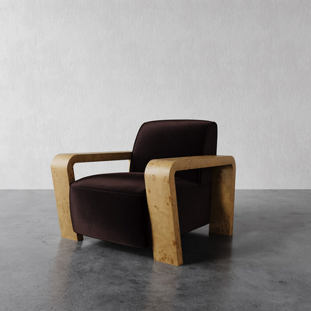 Lemieux et Cie Dumas Lounge Chair with dark brown upholstery and curved blonde frame, shown on polished concrete floor against neutral plaster walls.