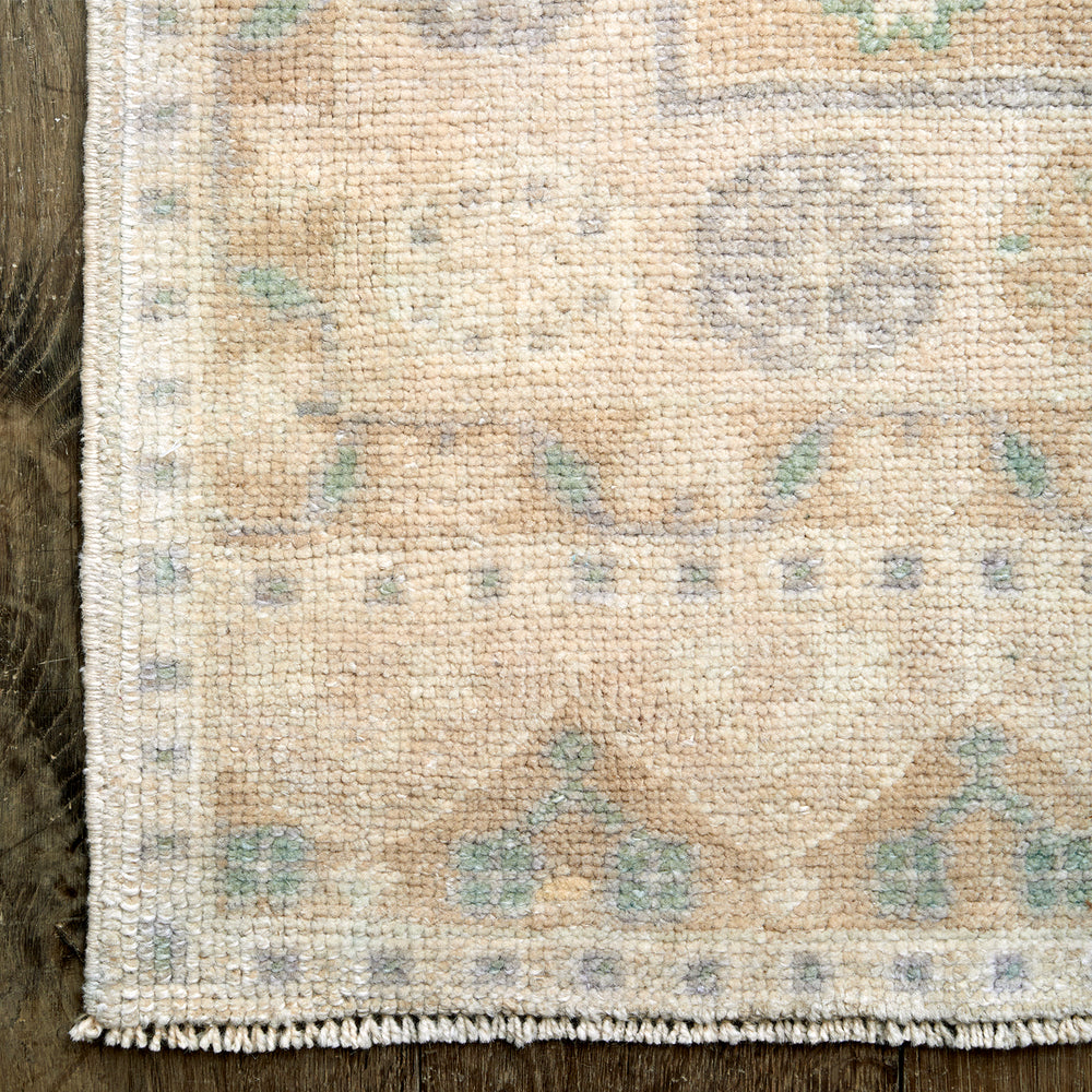 Lemieux et Cie Anatolian Village Rug in soft ivory, peach, sage and grey geometric pattern, handwoven vintage Turkish rug on dark wood flooring.