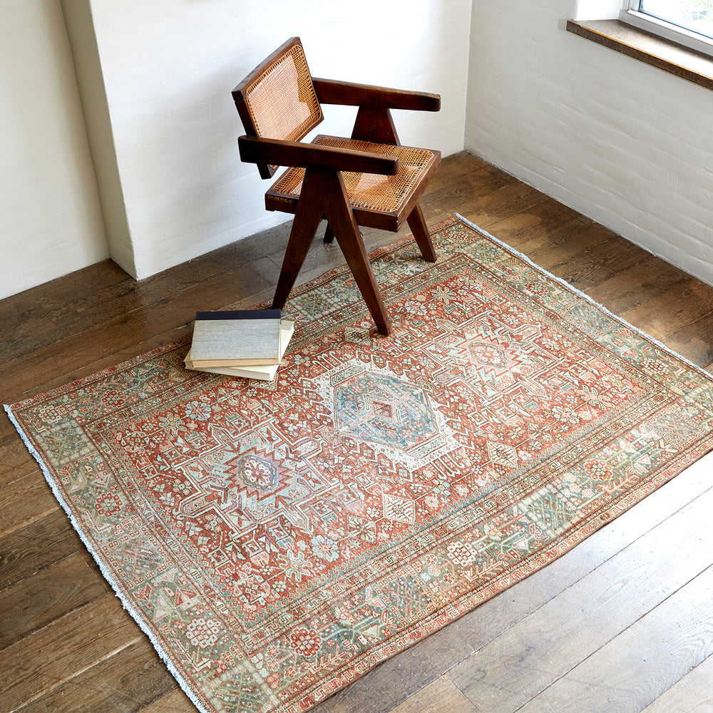 Lemieux et Cie Heriz Carpet in rust, blue and green, vintage Persian rug with geometric medallion pattern, shown with cane chair on wood floors in white-walled room.