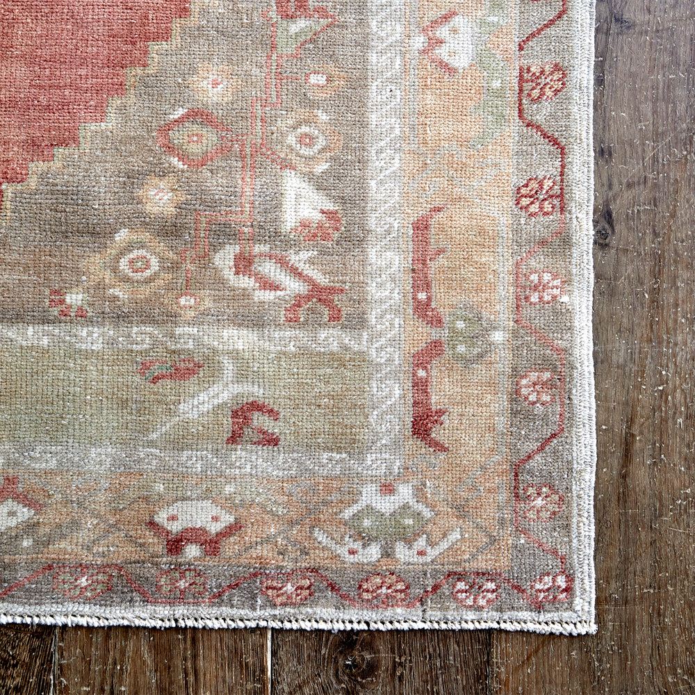Lemieux et Cie Anatolian Village Rug in coral, taupe and ivory wool, vintage Turkish rug with geometric motifs shown on weathered wood flooring.