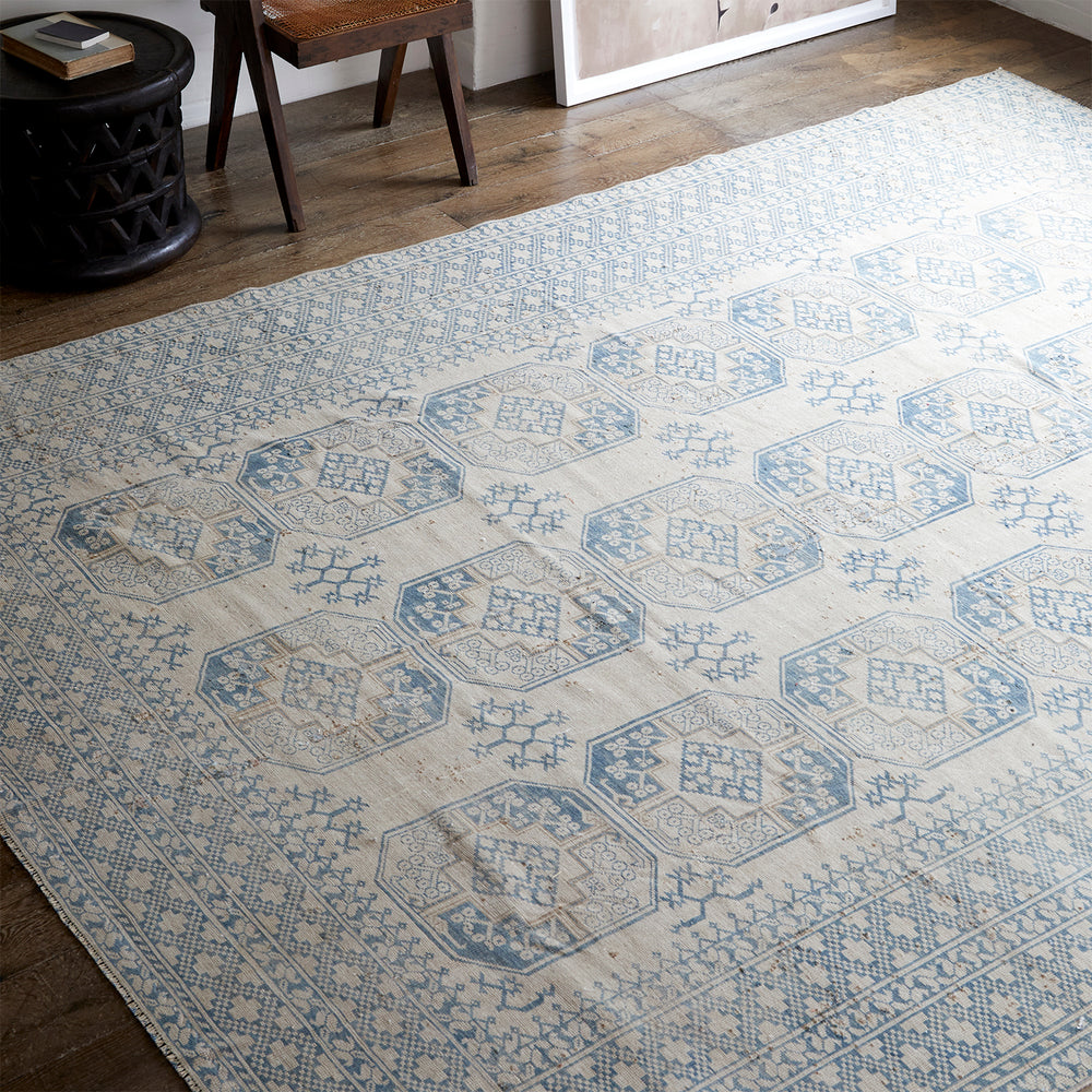 Lemieux et Cie vintage Persian rug in ivory and blue geometric medallion pattern, handwoven circa 1960, shown on wood floors beside dark carved side table.