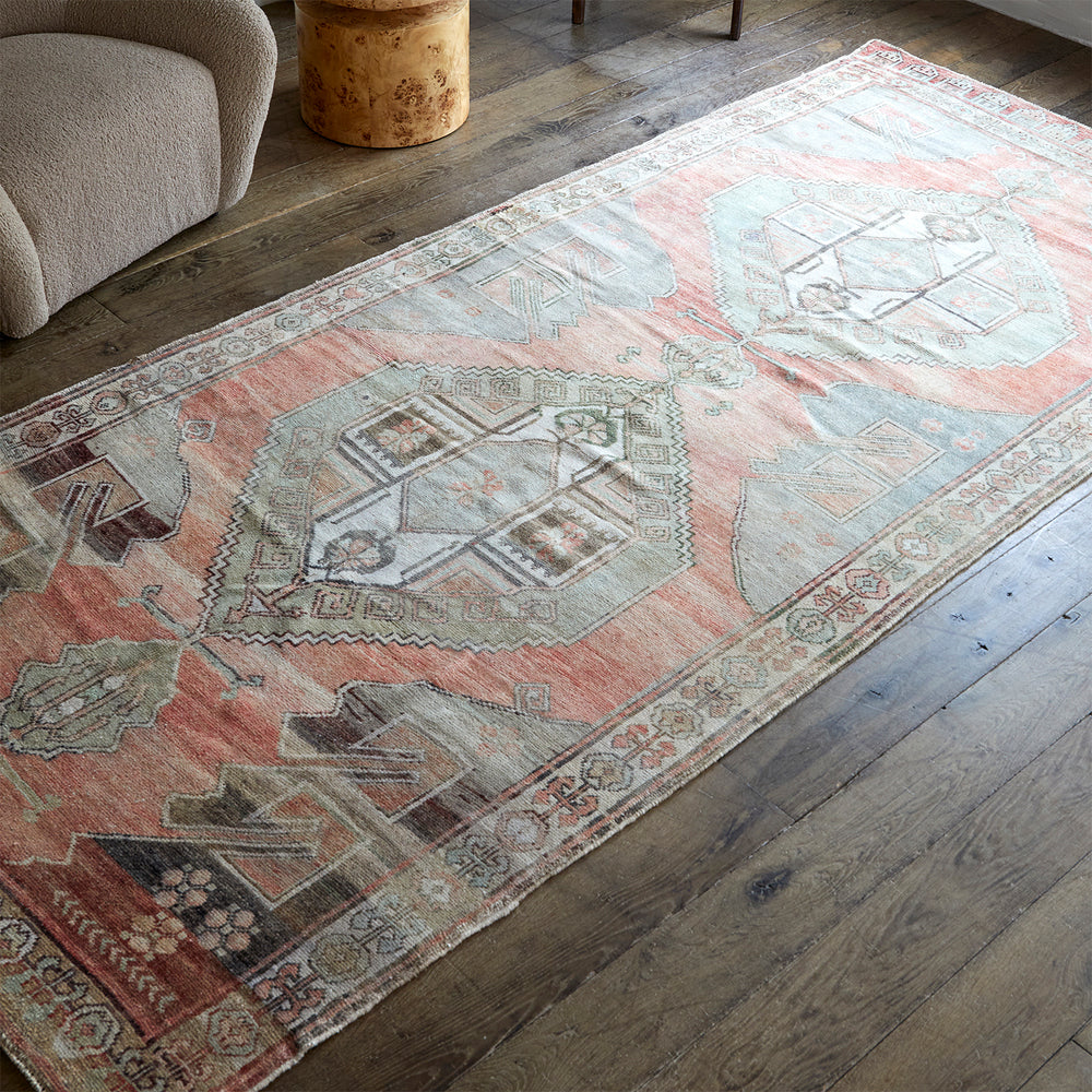 Lemieux et Cie Anatolian village rug in soft pink, blue and taupe geometric pattern, vintage wool rug on weathered wood floors beside textured seating.