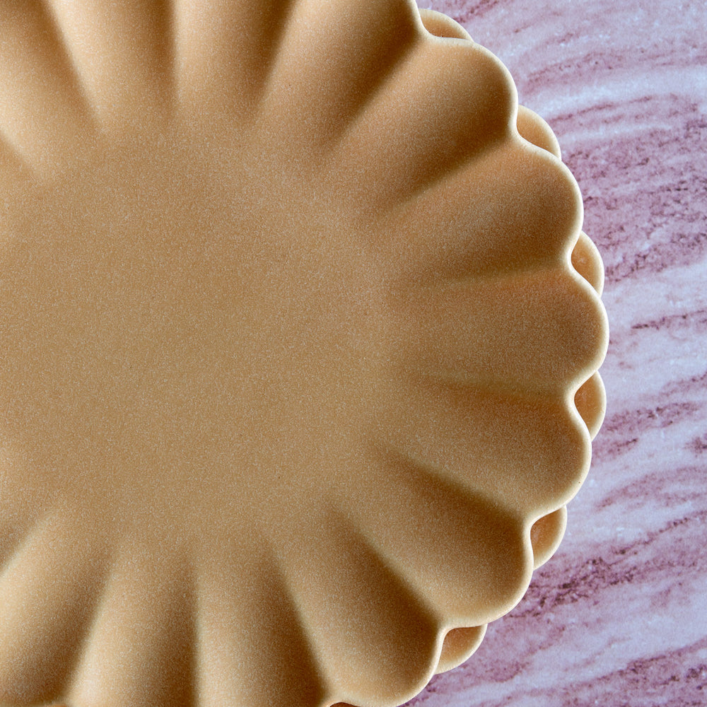 Lemieux et Cie Dhalia Stoneware Dinner Plate in camel, scalloped ceramic dinnerware shown on veined marble surface in warm natural light.