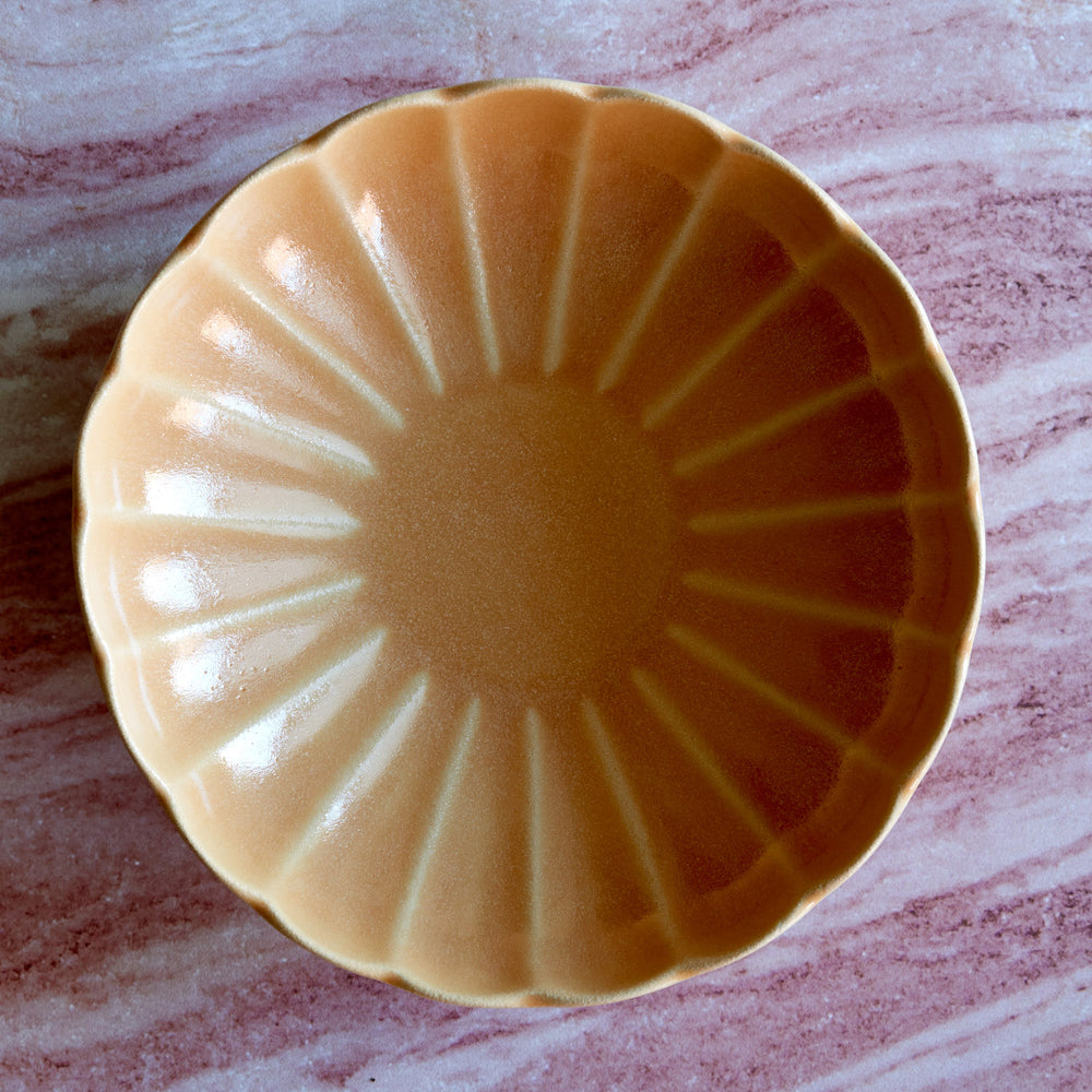 Lemieux et Cie Dhalia Stoneware Pasta Bowl in camel, scalloped ceramic bowl with ribbed detail, shown on pink-veined marble surface.