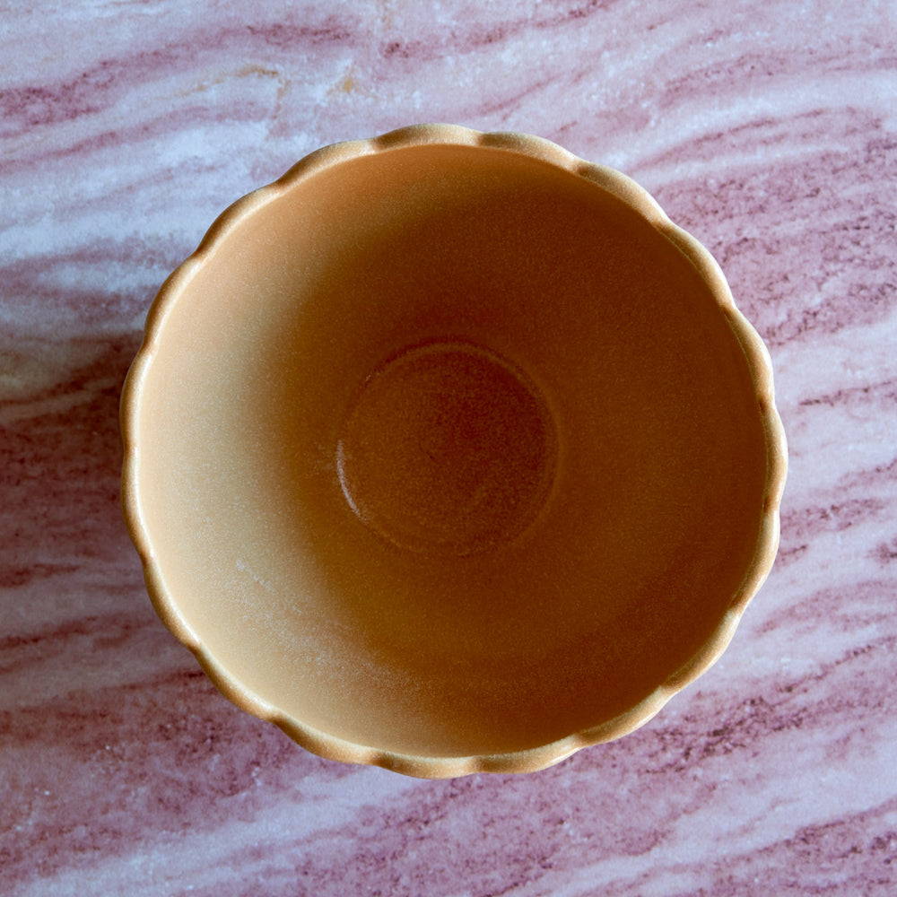Lemieux et Cie Dhalia Stoneware Bowl in camel, scalloped ceramic bowl shown overhead on pink-veined marble surface.