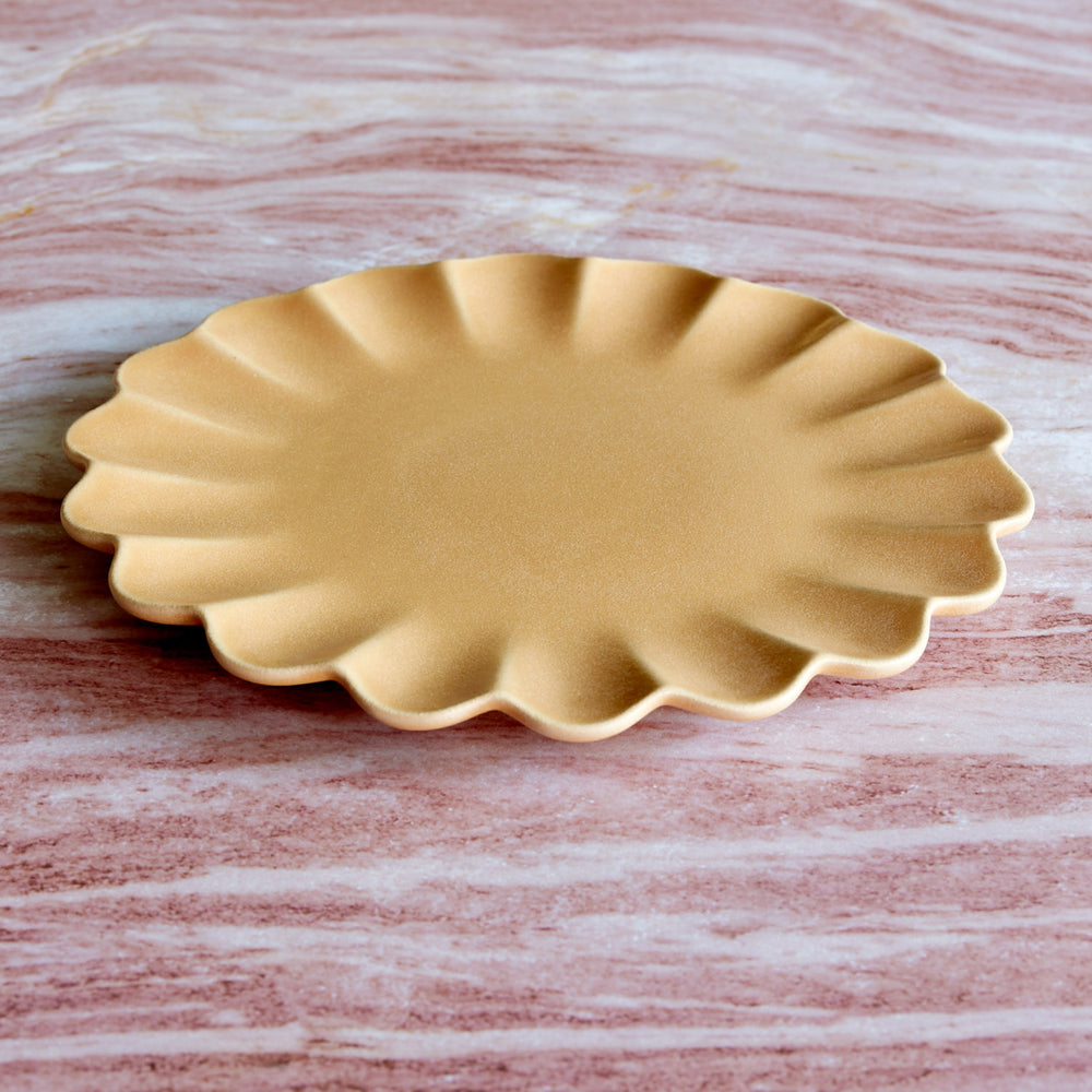 Lemieux et Cie Dhalia Stoneware Dinner Plate in camel, scalloped ceramic plate with fluted edges, shown on pale marble surface.