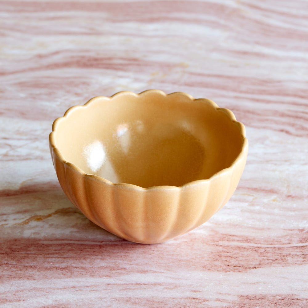 Lemieux et Cie Dhalia Stoneware Bowl in camel, scalloped ceramic bowl with fluted edges, shown on weathered stone surface with warm light.