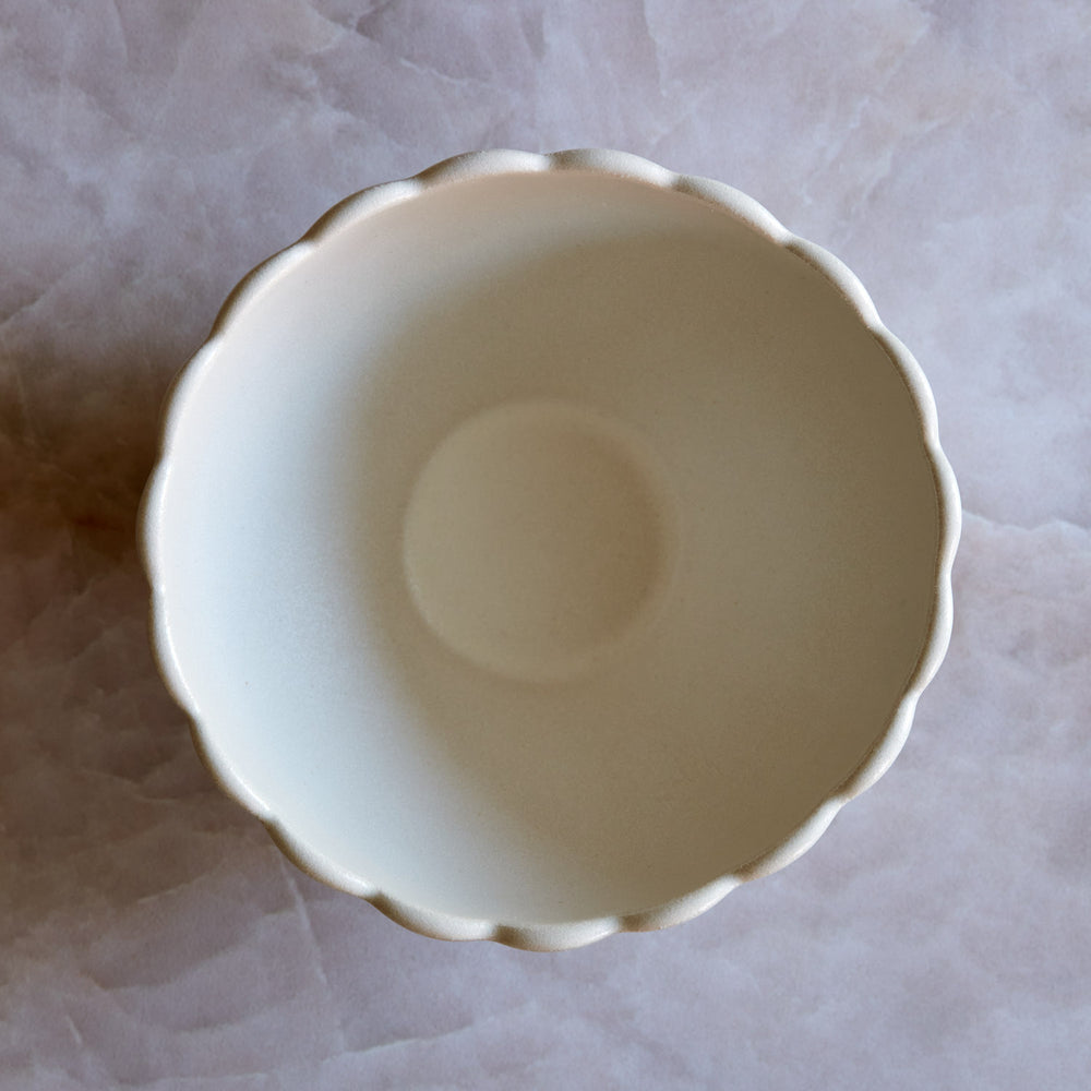 Lemieux et Cie Dhalia Stoneware Bowl in white, ceramic bowl with scalloped rim shown from above on pale marble surface.