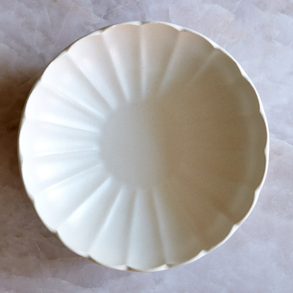 Lemieux et Cie Dhalia Stoneware Pasta Bowl in white, scalloped ceramic bowl with fluted interior, held above light stone surface.
