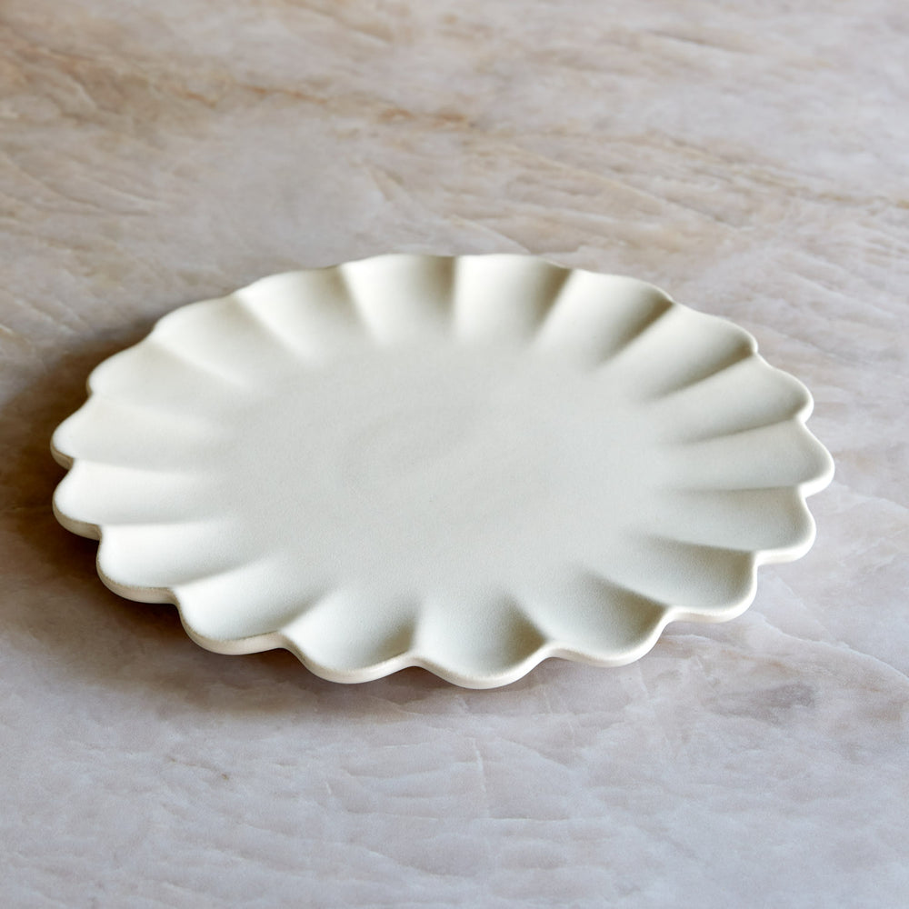 Lemieux et Cie Dhalia Stoneware Dinner Plate in white, scalloped ceramic plate with organic petal-shaped edge, shown on pale stone surface.