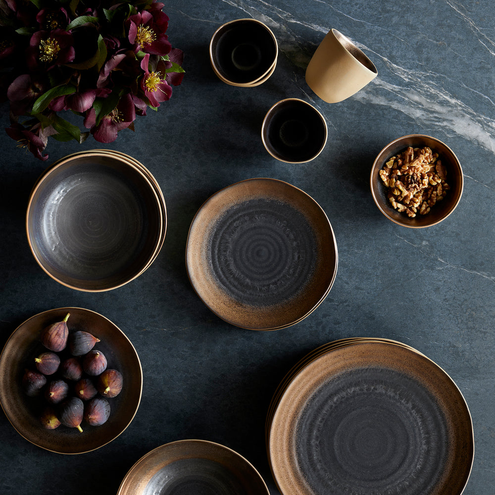Lemieux et Cie Akita Stoneware dinnerware set with warm bronze and charcoal glazed ceramic pieces arranged on dark stone surface with fresh figs and walnuts