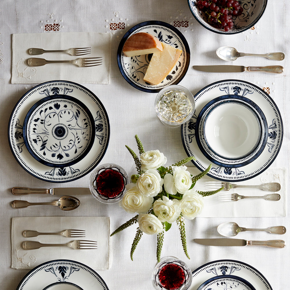 Lemieux et Cie Bruges Porcelain dinnerware set with hand-painted blue and white floral motifs, shown on white linen tablecloth with flatware and fresh flowers.