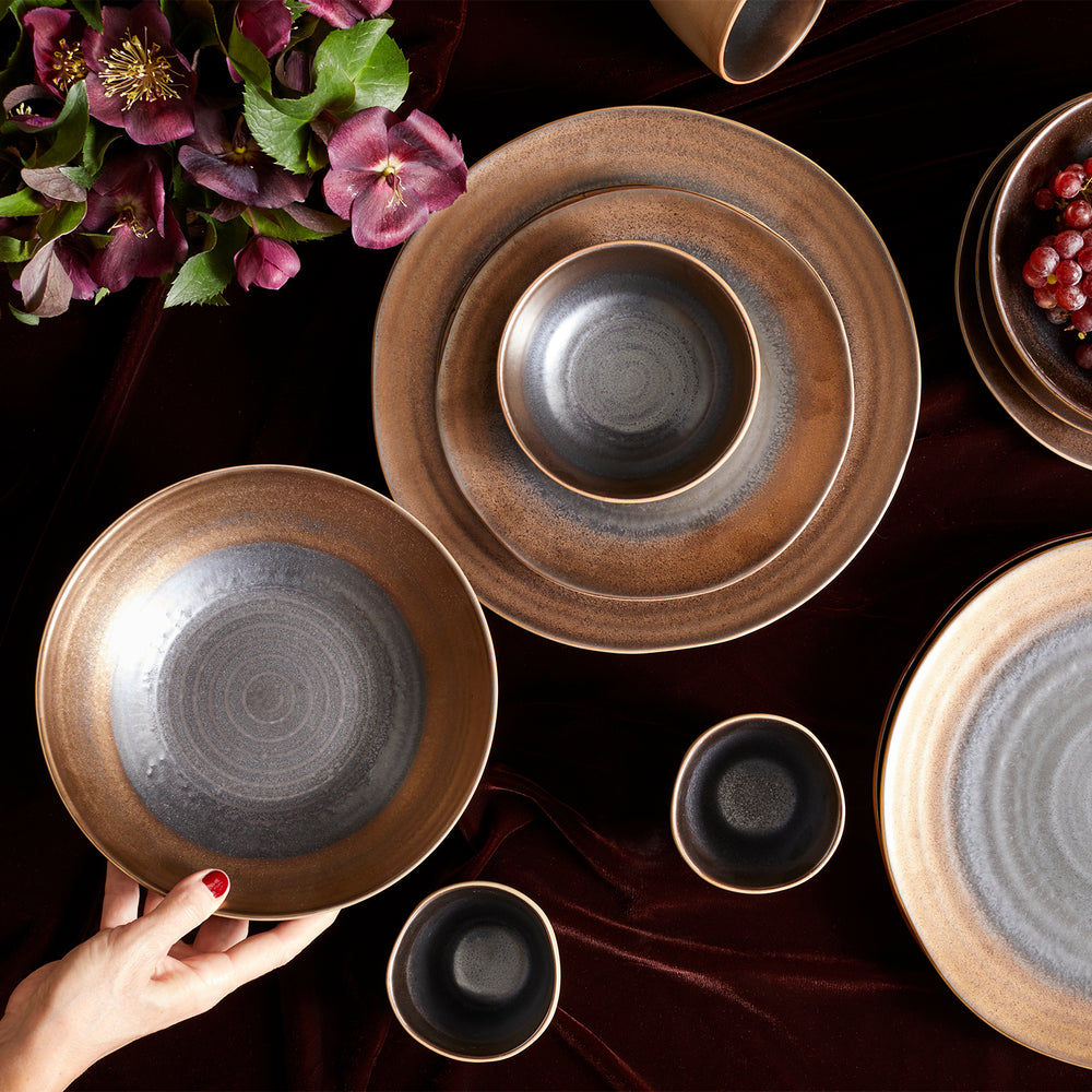 Lemieux et Cie Akita Stoneware dinnerware set in warm brown and charcoal glaze, ceramic plates and bowls arranged on dark velvet with burgundy hellebore blooms.