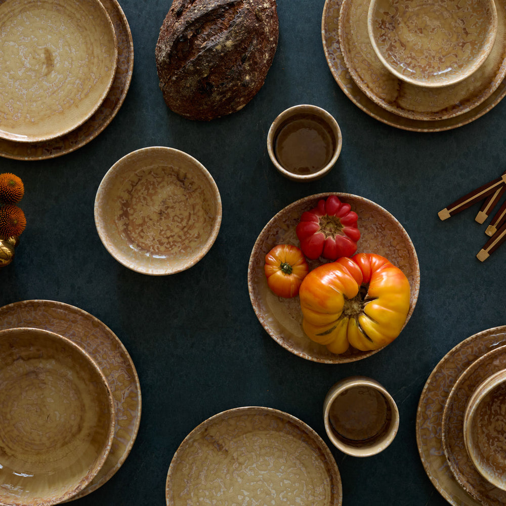Lemieux et Cie Hanami Stoneware Dinnerware Set in Sand, ceramic plates and bowls with reactive glaze, arranged on dark teal surface with heirloom tomatoes.