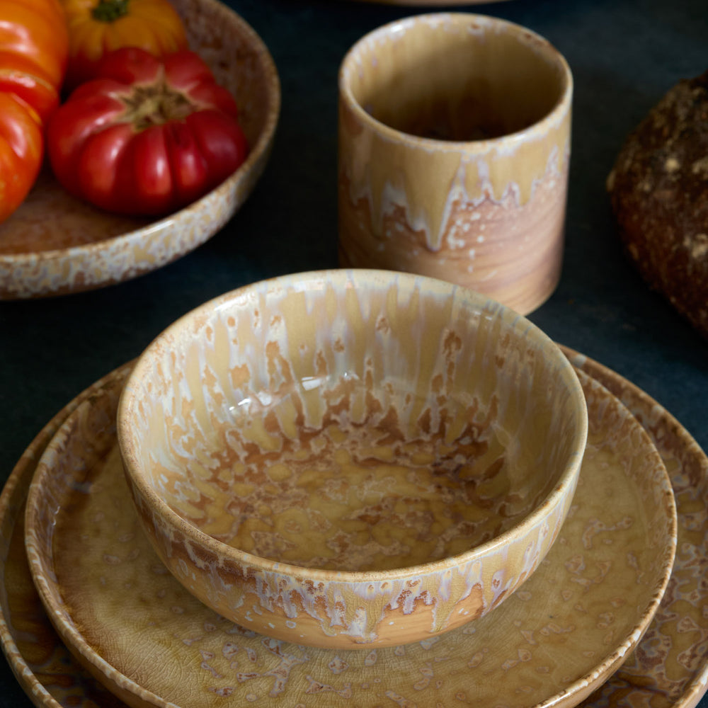 Lemieux et Cie Hanami Stoneware Salad Plate Set in Sand with reactive glaze, ceramic dinnerware stacked with bowl and tumbler, styled with heirloom tomatoes on dark surface.