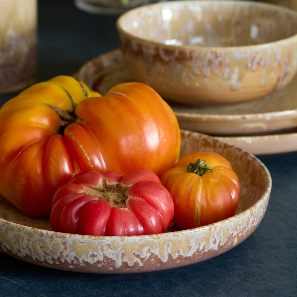 Lemieux et Cie Hanami Stoneware Dinnerware in sand reactive glaze, ceramic bowls and plates holding heirloom tomatoes on dark table surface.