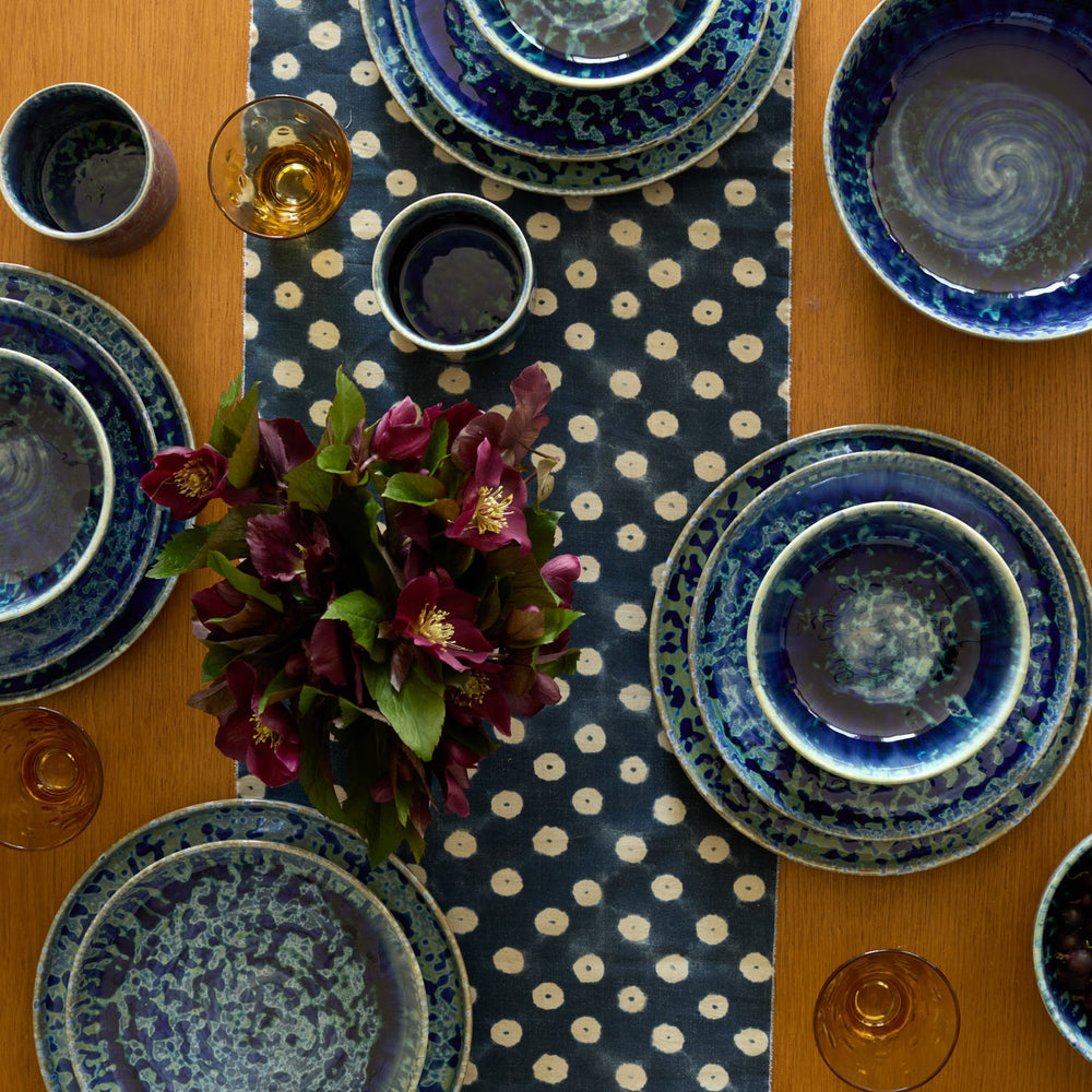 Lemieux et Cie Hanami Stoneware Dinnerware Set in indigo with reactive glaze, ceramic plates and bowls arranged on polka dot runner atop wood dining table.