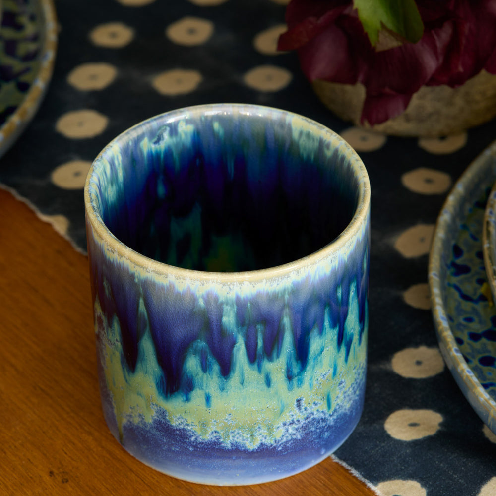 Lemieux et Cie Hanami Stoneware mug in indigo reactive glaze, cylindrical ceramic vessel with blue-green gradient, shown on dark patterned rug.