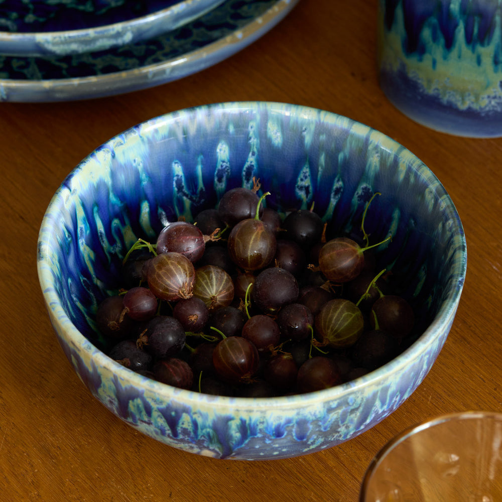 Lemieux et Cie Hanami Stoneware Bowl in indigo reactive glaze holding fresh berries, shown on warm wood table with additional bowls.