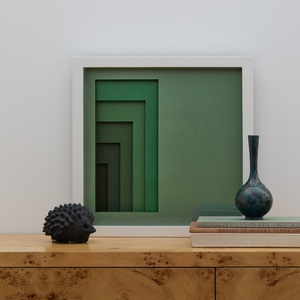Lemieux et Cie Composition Tonale No. 3, geometric stepped relief in sage green tones, displayed on burl wood cabinet in neutral-walled room.