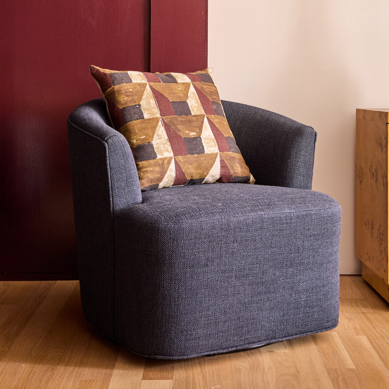 Lemieux et Cie Garnier Swivel Chair in navy, rounded lounge chair with geometric pillow, on wood floor against red and neutral walls.