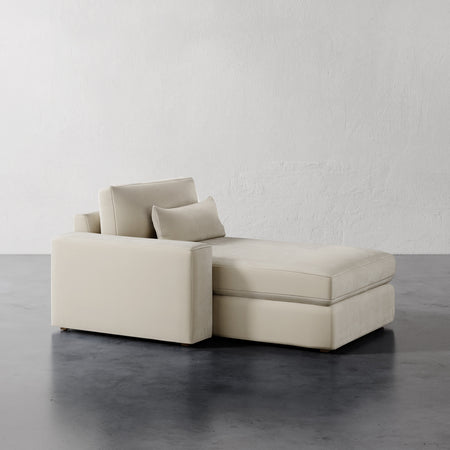 Lemieux et Cie Lacroix Left or Right Chaise & A Half in ivory, modular sectional with ottoman, shown on dark concrete floor against white plaster wall.