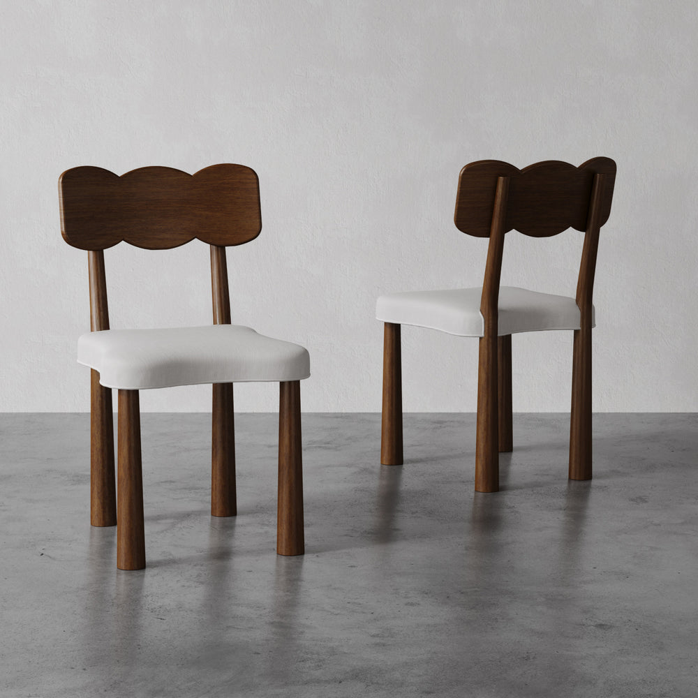 Lemieux et Cie Madeleine Dining Chair in walnut oak with ivory upholstered seat, sculptural bow-shaped back, shown on polished concrete floor against neutral walls.