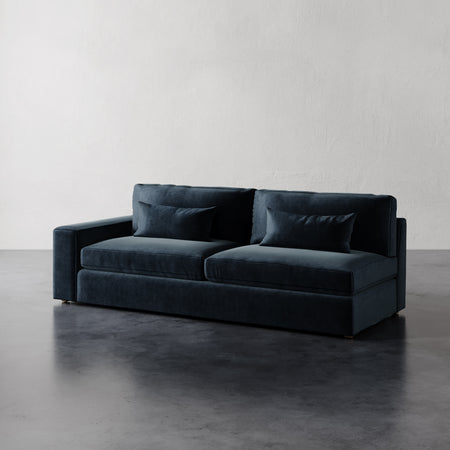 Lemieux et Cie Lacroix Left Arm Sofa in deep blue, tailored modular sofa with bolster pillows, shown on dark concrete floor against textured plaster walls.
