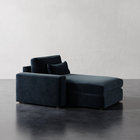 Lemieux et Cie Lacroix Left or Right Chaise & A Half in deep teal velvet, modular chaise lounge on dark concrete floor against textured white walls.