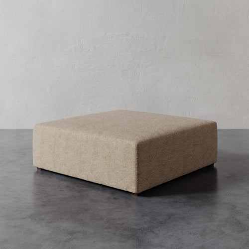 Lemieux et Cie Fabien 48" Square Ottoman in warm neutral, low-profile square ottoman on polished concrete floor against textured plaster walls.