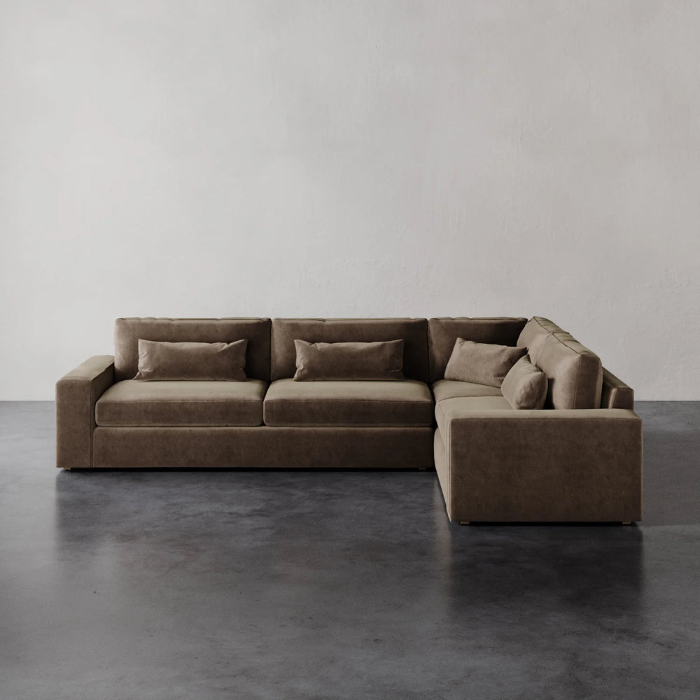Lemieux et Cie Lacroix Left Arm Sectional in warm taupe, modular sofa with bolster pillows, shown on dark concrete floor against neutral plaster walls.