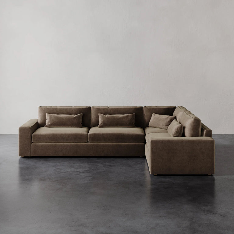 Lemieux et Cie Lacroix Left Arm Sectional in warm taupe, modular sofa with bolster pillows, shown on dark concrete floor against neutral plaster walls.