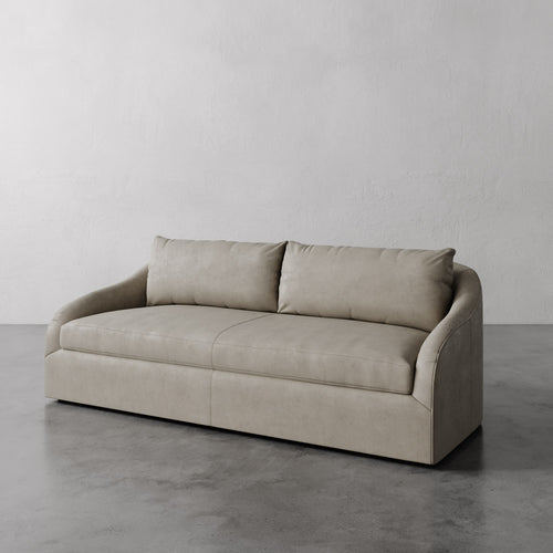 Lemieux Et Cie Light Gray Rousseau Leather Sofa on a gray floor with a plain white wall background.