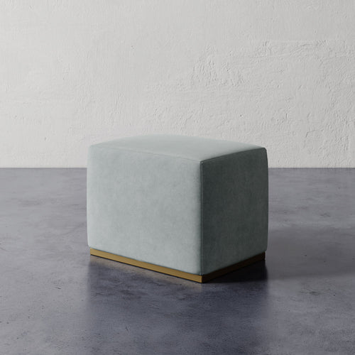 Lemieux et Cie Sophie Rectangular Ottoman in soft sage upholstery with brass base, compact rectangular ottoman on concrete floor against textured plaster wall.
