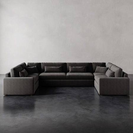 Lemieux et Cie Lacroix U-Sectional in charcoal, modular sofa with rectilinear lines and bolster pillows, shown on dark concrete floor against neutral walls.