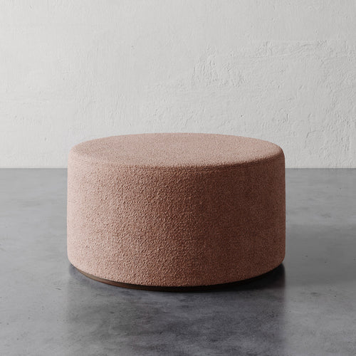 Lemieux et Cie Sophie Round 36" Ottoman in blush bouclé, cylindrical upholstered ottoman on concrete floor against textured plaster walls.