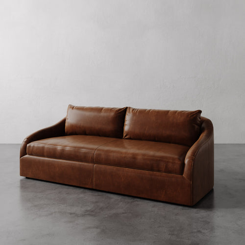 Lemieux Et Cie Brown Rousseau Leather Sofa on a gray floor with a plain white wall background.