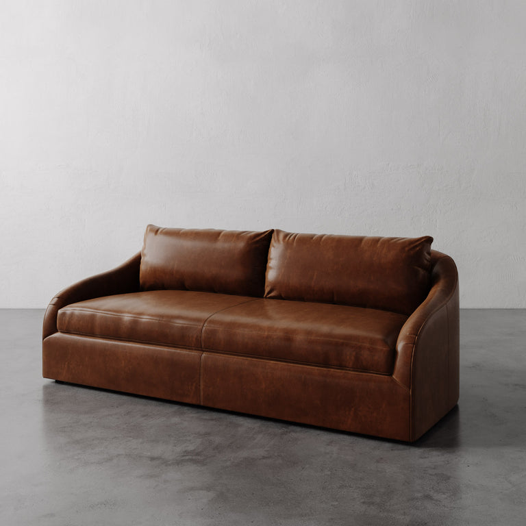 Lemieux Et Cie Brown Rousseau Leather Sofa on a gray floor with a plain white wall background.