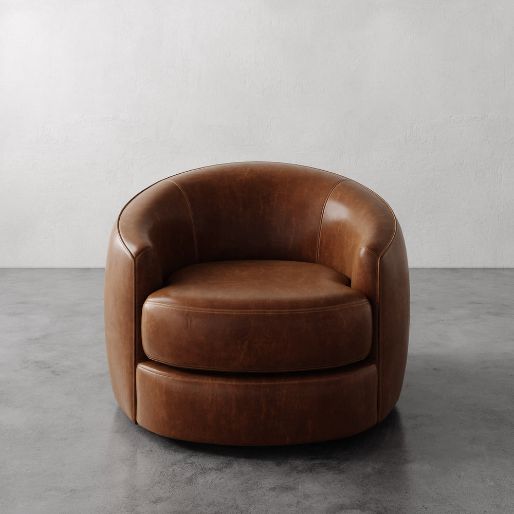 Lemieux et Cie Rulmann Swivel Chair in warm tobacco leather, rounded barrel-back form, shown on concrete floor against neutral plaster walls.