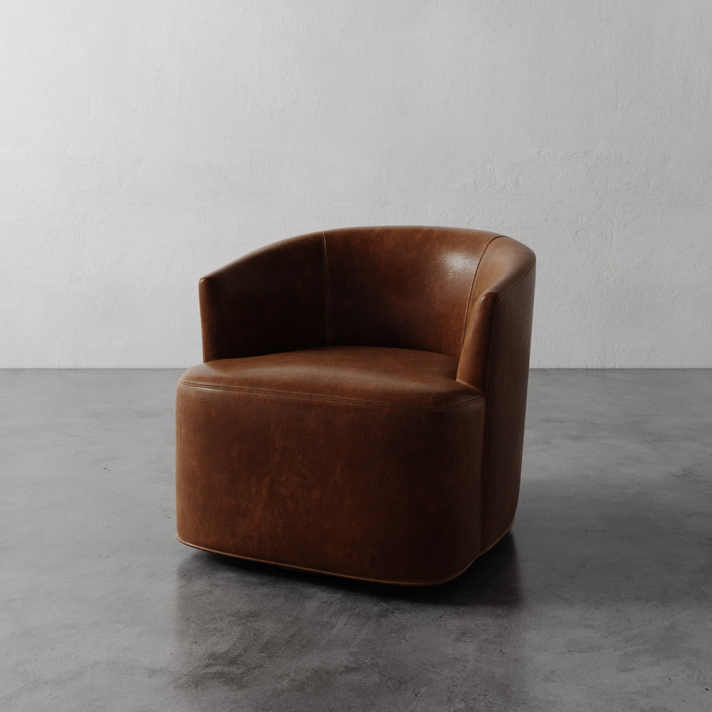 Lemieux et Cie Garnier Swivel Chair in warm tobacco, rounded barrel-back form, shown on polished concrete floor against white plaster walls.