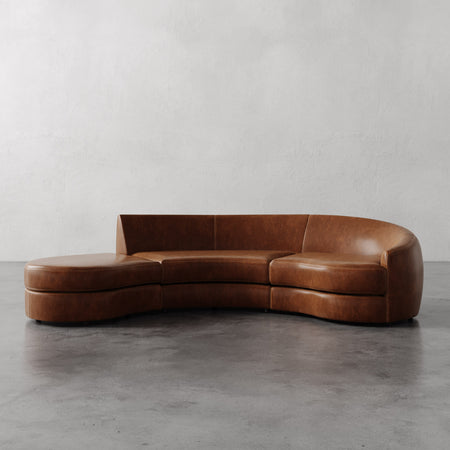 Lemieux et Cie Rulmann 3-Piece Right Sectional in warm cognac leather, curved sculptural sofa on polished concrete floor against neutral plaster walls.