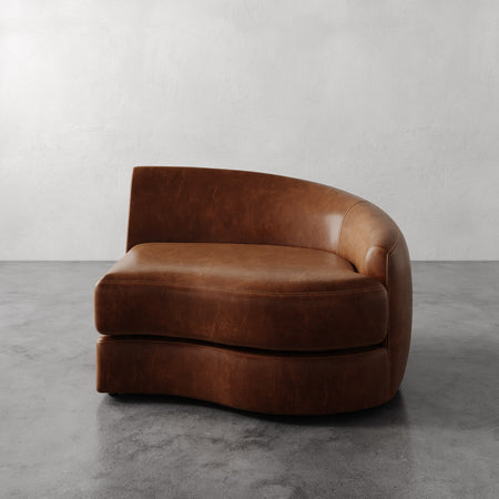 Lemieux et Cie Rulmann Right Arm Chair in warm brown leather, curved low-profile lounge chair on concrete floor against white walls.