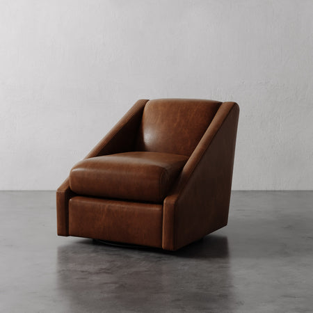 Lemieux et Cie Fontaine Swivel Chair in warm brown leather, low-profile lounge chair with angular sloped arms on concrete floor with textured plaster walls.