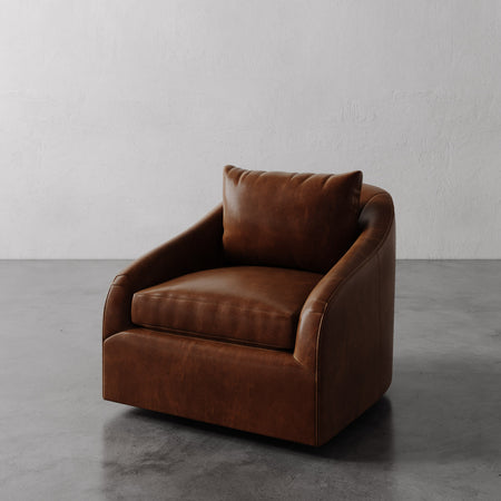 Lemieux et Cie Rousseau Swivel Chair in warm cognac leather, low-profile lounge chair with rounded arms, shown on concrete floor against white wall.