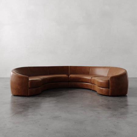Lemieux et Cie Rulmann curved leather sectional in warm cognac tones, shown on polished concrete floor against neutral plaster walls.