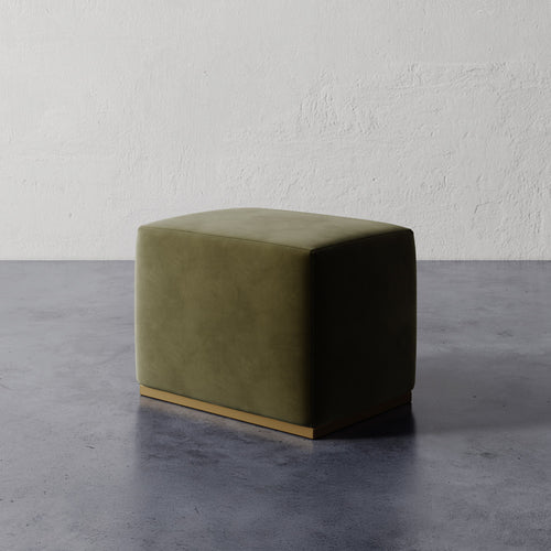 Lemieux et Cie Sophie Rectangular Ottoman in olive green upholstery, low-profile ottoman with brass base, shown on concrete floor against textured plaster wall.