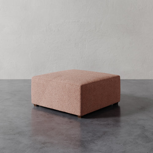 Lemieux et Cie Fabien 36" Square Ottoman in blush textured upholstery, low-profile ottoman on stone floor against textured plaster walls.