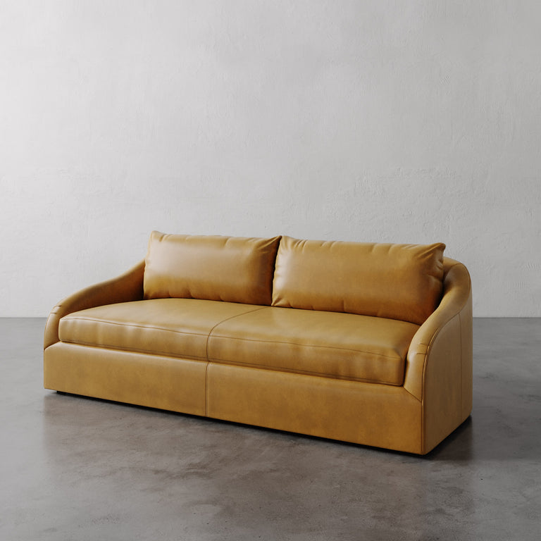Lemieux Et Cie Tan Rousseau Leather Sofa on a gray floor with a plain white wall background.