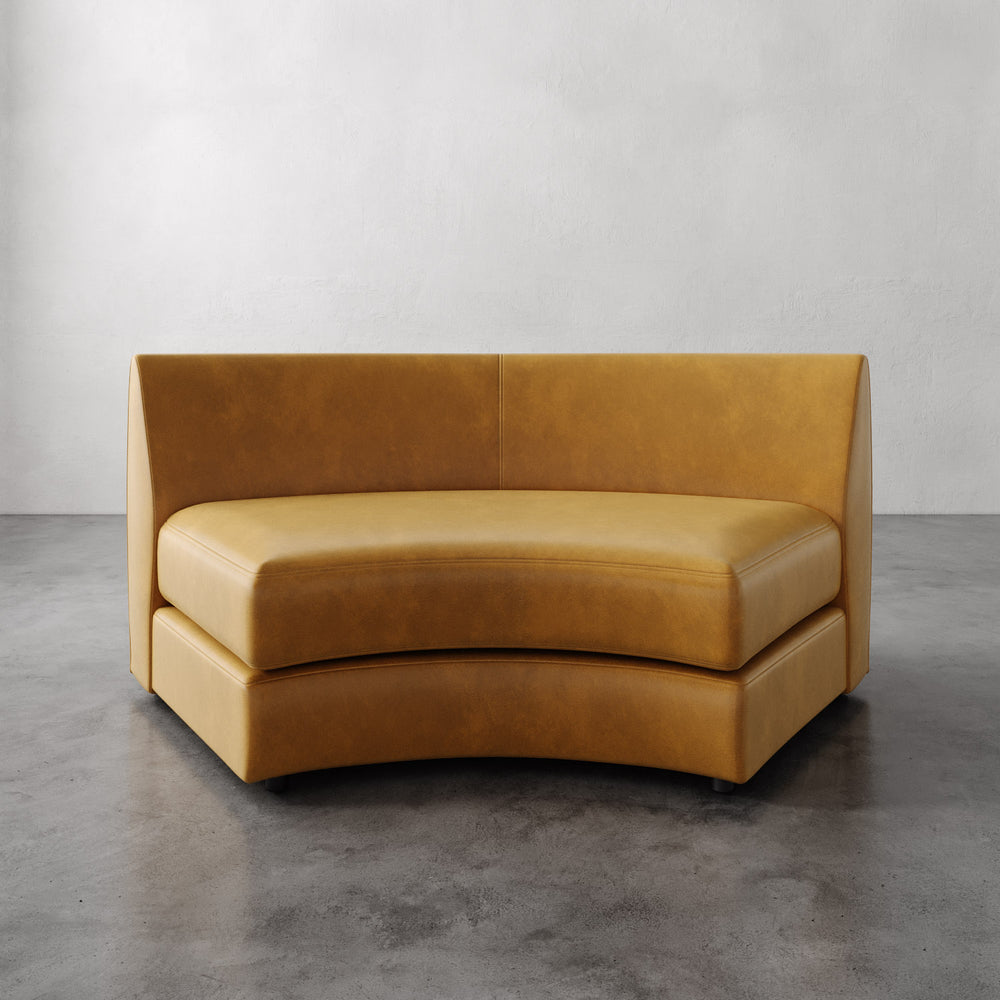 Lemieux et Cie Rulmann Wedge in warm tobacco leather, curved sectional sofa with high back, shown on polished concrete floor against white walls.