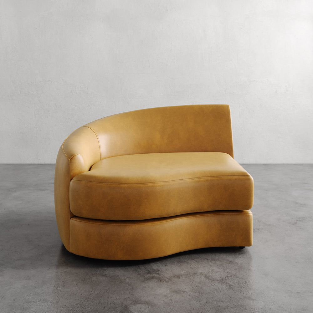 Lemieux et Cie Rulmann Left Arm Chair in warm tobacco leather, curved sectional seating with organic sculptural form, shown on concrete floor against white walls.
